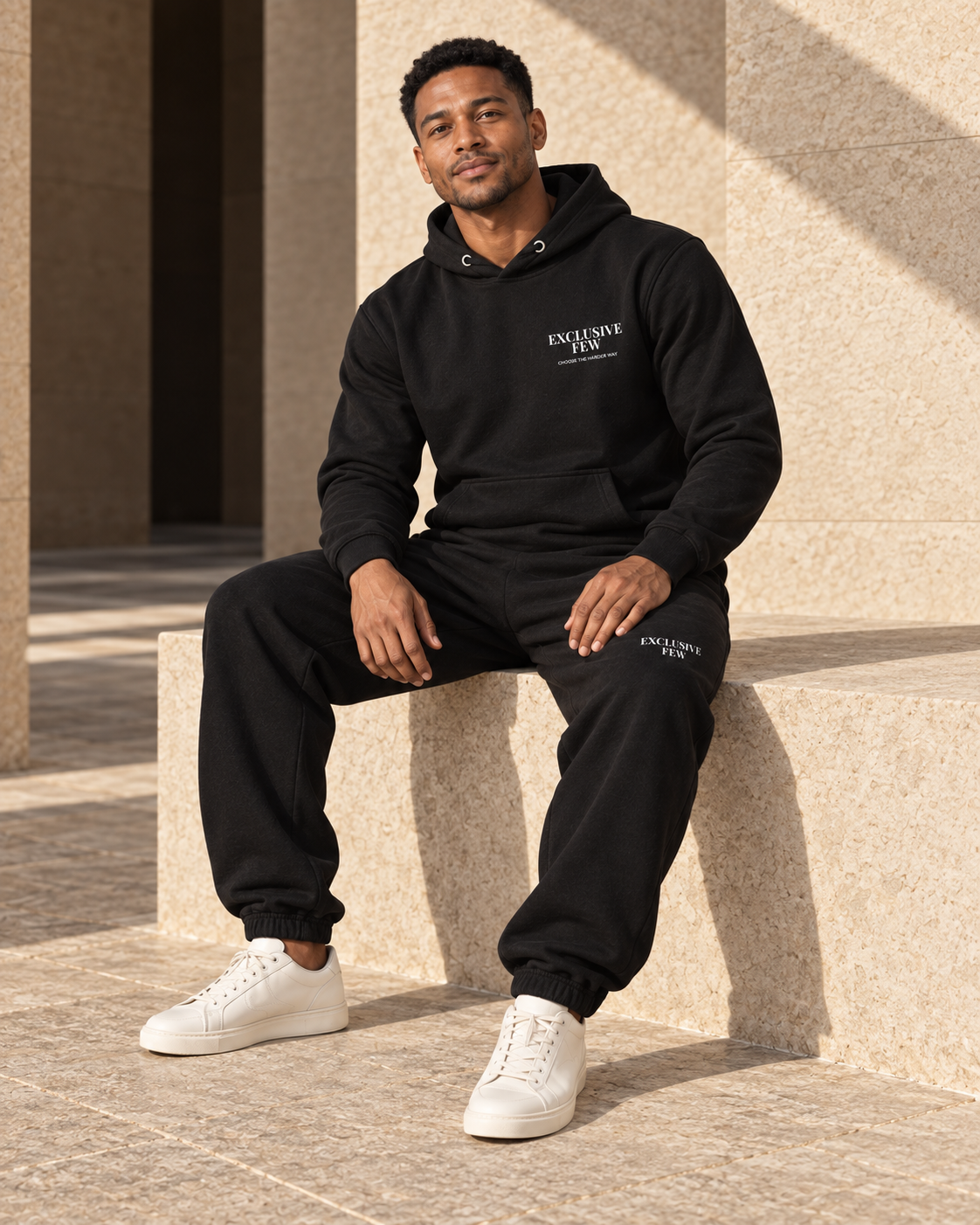 Model seated in the black Signature Hoodie with matching black sweatpants.