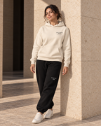Model wearing the bone Signature Hoodie with black sweatpants beside a stone column.