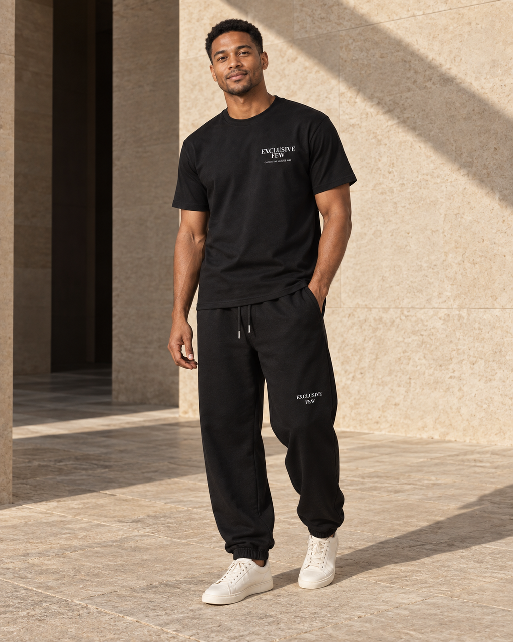 Model wearing the black Signature Tee with matching black sweatpants in a stone courtyard.